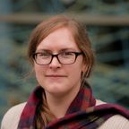 Head shot of Frances Turner, smiling, with long auburn hair and black-rimmed glasses, wearing a red tartan scarf.
