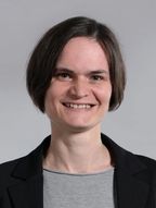 Head shot of Alice Gruber, smiling, with short brown hair, wearing a black blazer over a grey top.