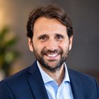 Head shot of Fabio Ruggiano, smiling, with dark hair and a beard, wearing a navy blazer and light blue shirt.